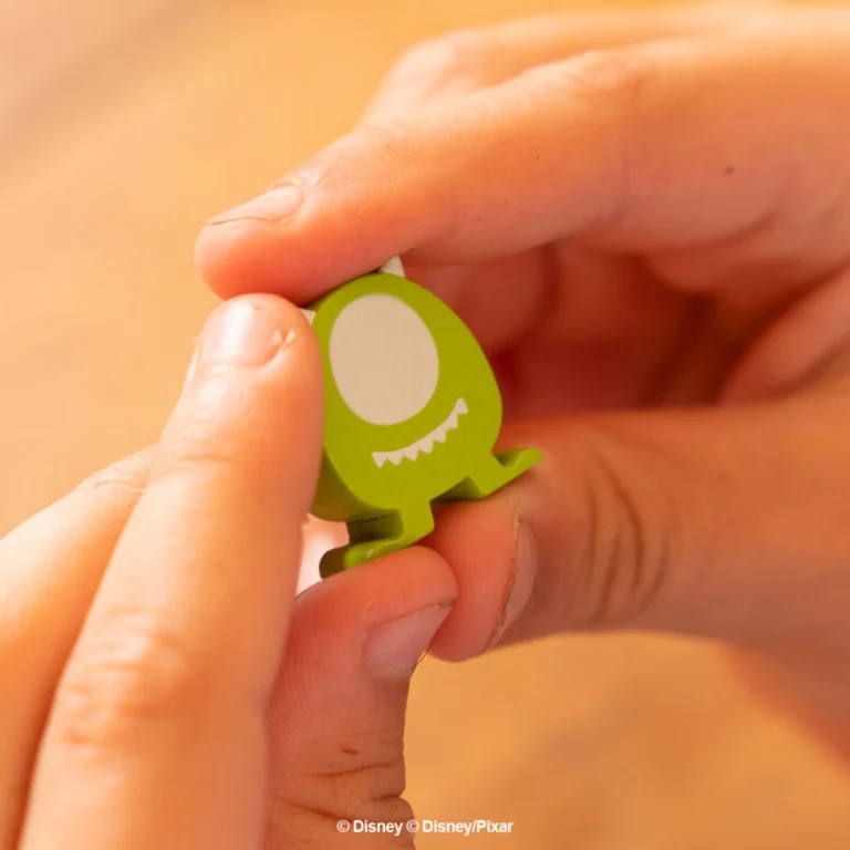 Duas mãos segurando a peça de personagem Mike Wazowski do Dixit Disney