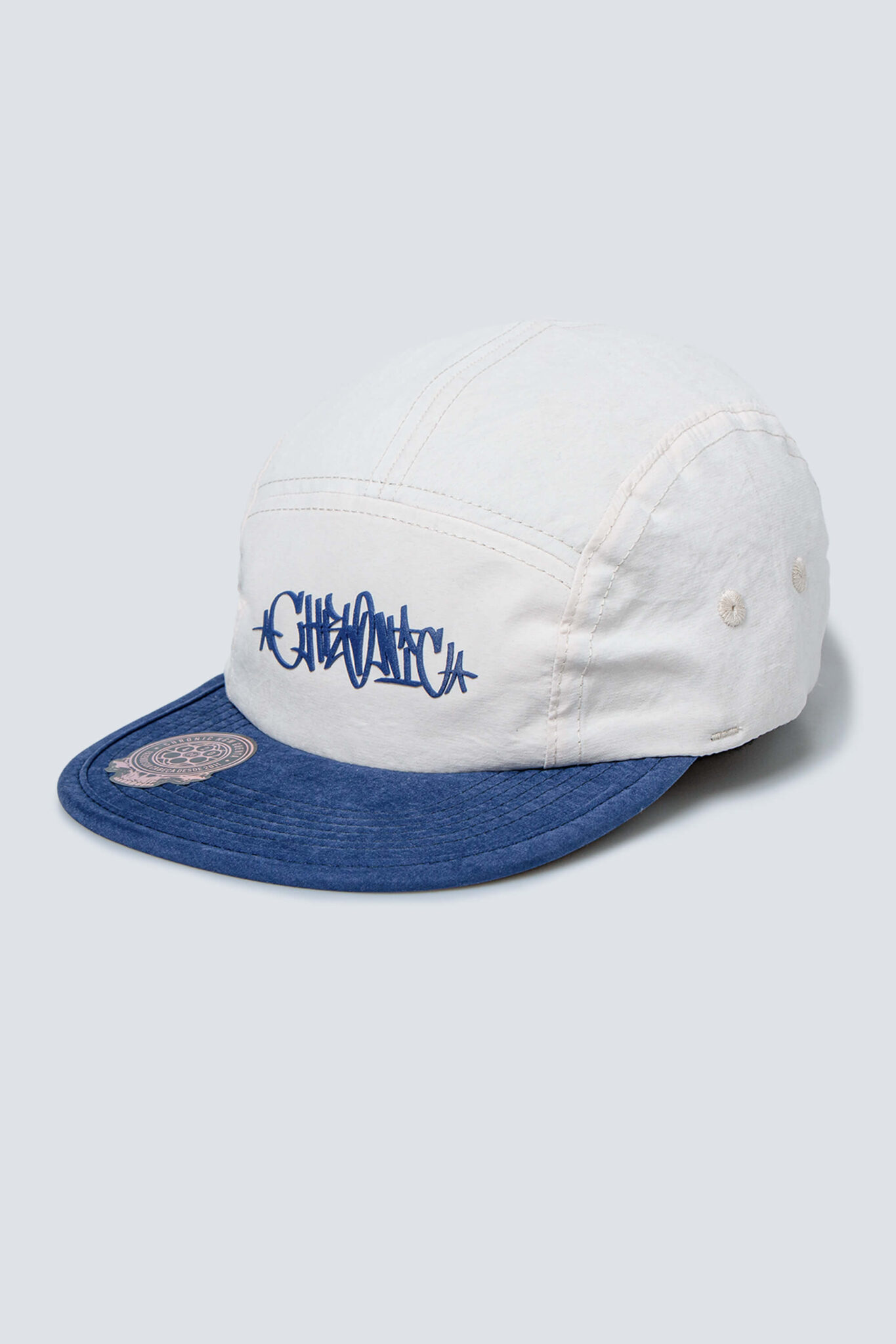 Boné cor areia da Chronic com aba de sarja aveludada e estampas em azul, visto de frente levemente inclinado para a esquerda.