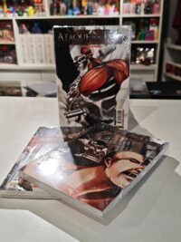 Três primeiros volumes do mangá Ataque dos Titãs empilhados, com dois deitados e um em pé, mostrando as capas com Eren, Mikasa e o Titã de Ataque.