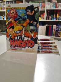 Um volume da edição Naruto Gold em pé na frente, com outros volumes empilhados atrás mostrando as laterais com os títulos e números das edições, destacando o acabamento diferenciado e a arte de Masashi Kishimoto na capa.