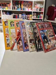 Sete volumes do mangá One Piece enfileirados em pé, mostrando as capas sequenciais com o protagonista Monkey D. Luffy em diferentes poses e expressões, arte característica de Eiichiro Oda, com fundos coloridos variando entre azul, vermelho e amarelo.